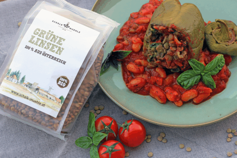 Vegane gefüllte Paprika mit Linsen und Gemüsefüllung auf Tomaten-weiße Bohnen-Sauce, mit frischen Cocktailtomaten, Basilikumblatt und Schalk Mühle Bio Grüne Linsen Packung.