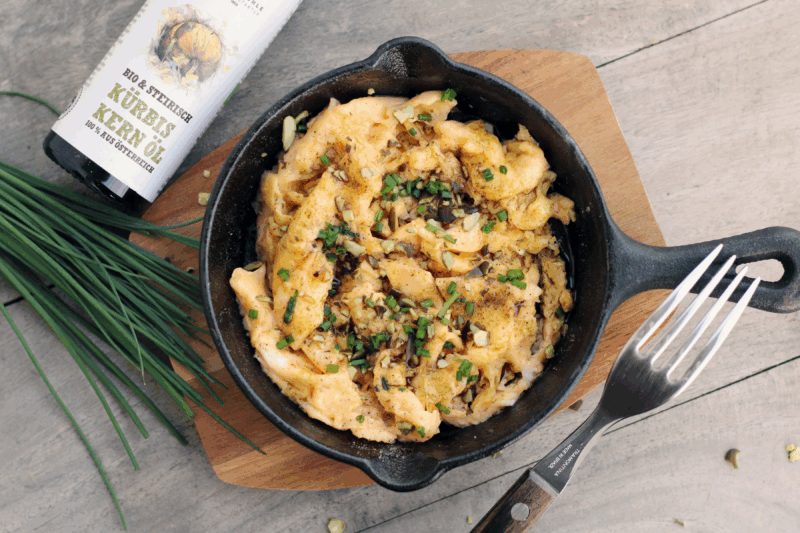 Steirische Eierspeise, ein cremiges Rührei mit steirischem Kürbiskernöl g.g.A. und Kürbiskernen der Schalk Mühle, serviert in einer gusseisernen Pfanne auf Holzbrett.