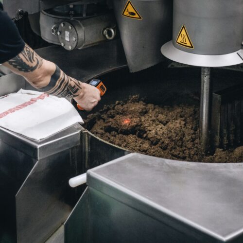 Ölpresse beim Messen der Temperatur, Ein Mann links stehend misst mit einem Gerät die Kürbiskern Masse in der Ölpresse