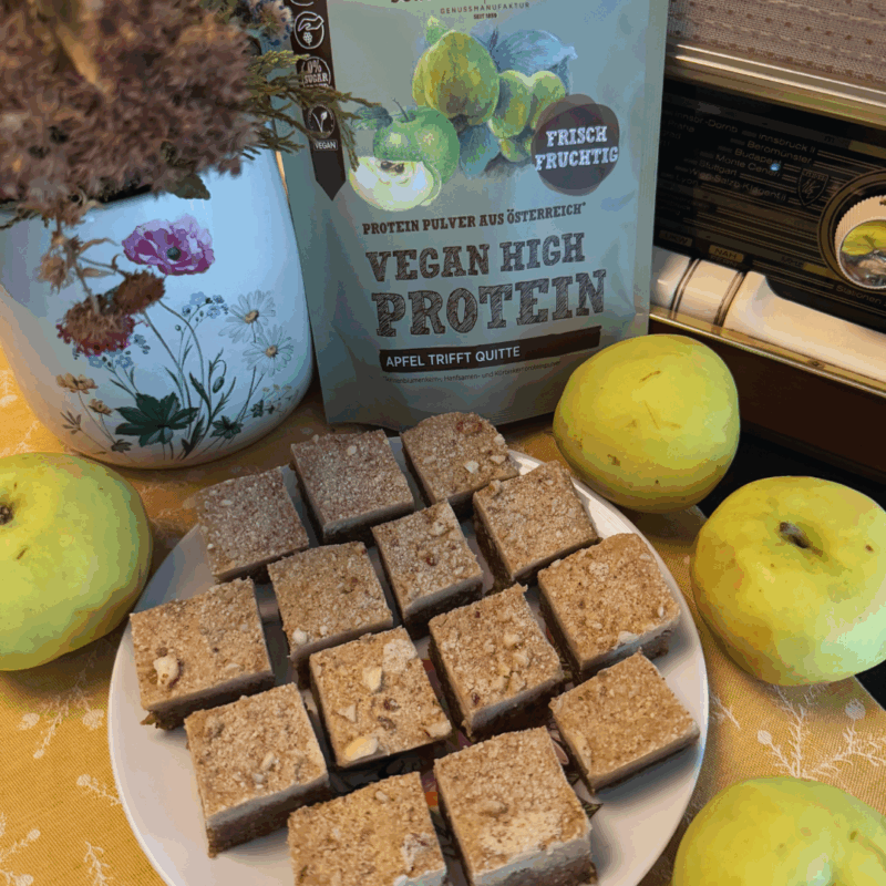 Gesunde vegane Apfelnuss-Wolken auf einem Teller, umgeben von frischen Äpfeln. Im Hintergrund ein Beutel Schalk Mühle Proteinpulver Apfel-Quitte und eine dekorative Blumenvase.