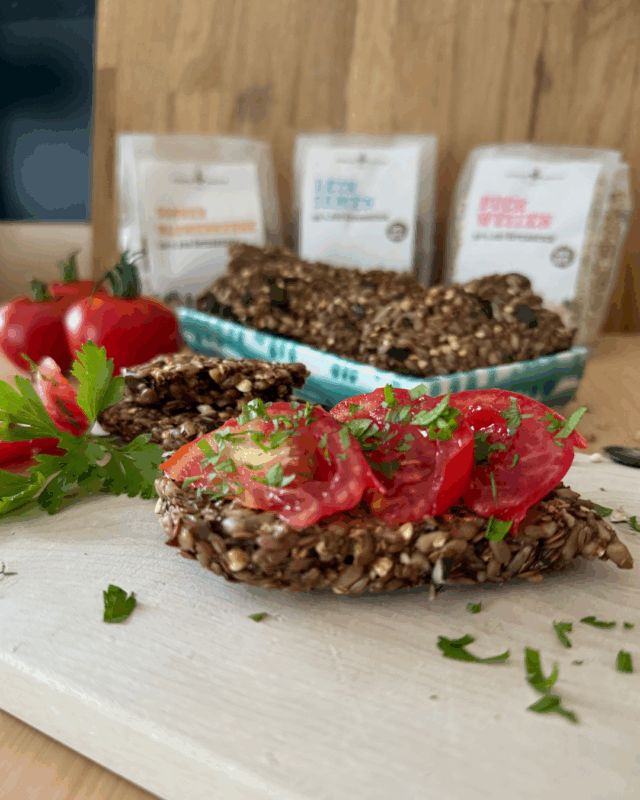 Glutenfreies Saatenbrot, mit Schalk Mühle Saaten und Kerne, Tomaten und Petersilien Garnitur, angerichtet auf einem Schneidebrett .