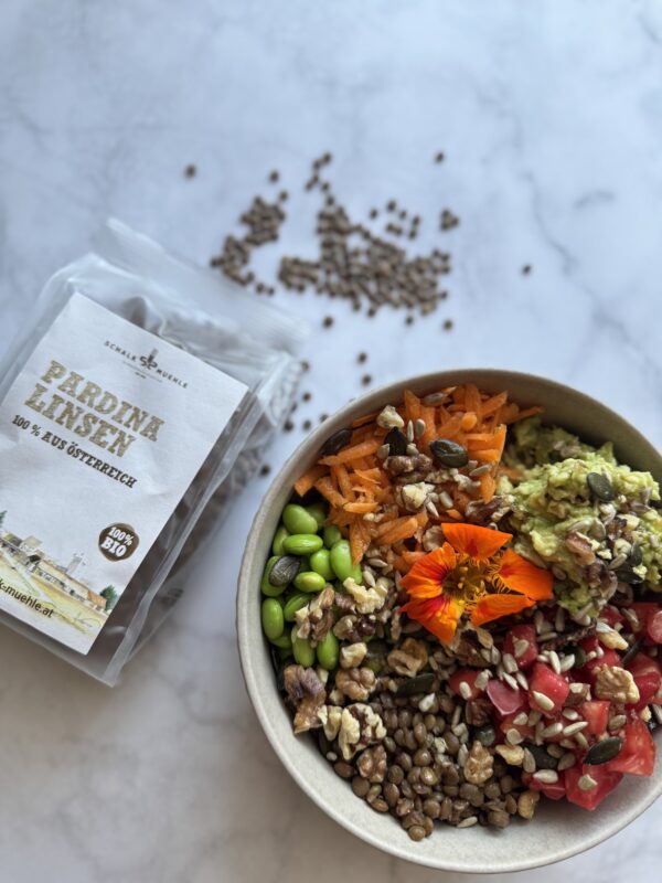 Pardina Linsen Salat, in einer Schüssel dekorativ angerichtet, mit Gemüse, Blüten - daneben eine Packung Pardina Linsen von Schalk Mühle