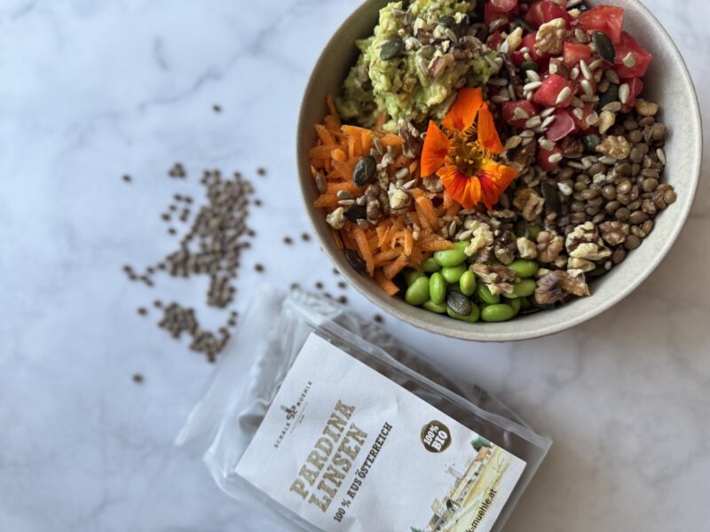 Pardina Linsen Salat, in einer Schüssel dekorativ angerichtet, mit Gemüse, Blüten - daneben eine Packung Pardina Linsen von Schalk Mühle